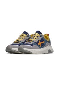 Sneakers con una combinazione di suede grigio e rete blu navy, lacci gialli e un grande accentuazione a stella arancione; suola spessa bianca con suola esterna grigia testurizzata.