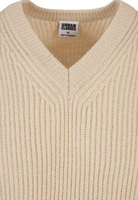 Beżowy sweter dziany z dekoltem w serek, z pionowymi detalami ribbingu oraz metką wskazującą rozmiar M i pochodzenie. Teksturowana tkanina.