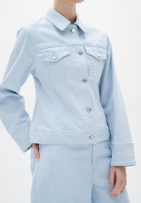 Gaišs zila denima jaka ar apkakles kaklu, priekšējo pogu aizdari, divām krūšu kabatām un pieguļošu siluetu ar izšūtiem akcentiem.