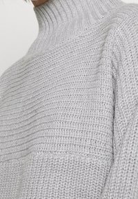 Pull gris clair en tricot avec un col montant côtelé, un motif texturé et une coupe décontractée avec épaules tombantes.