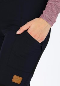 Navy dehnbare Hosen mit einer Seitentasche, versehen mit einem hellbraunen Lederpatch mit der Aufschrift "SWEDEMOUNT" nahe dem Saum, ergänzt durch einen strukturierten roten Oberarm.