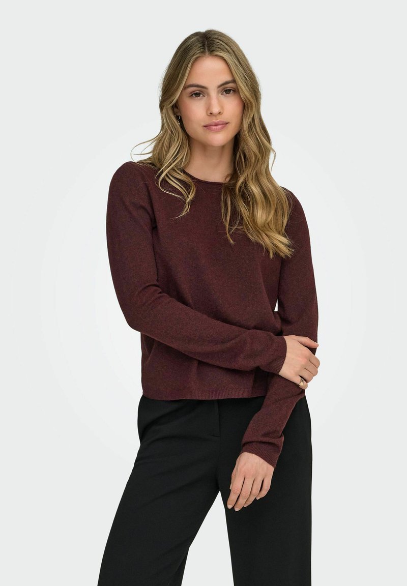 Suéter burdeos de manga larga, cuello redondo y ajuste relajado. Textura suave y diseño ligeramente corto, combinado con pantalones negros.