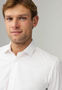 Chemise blanche avec un col classique, fermeture à boutons et texture lisse. Les tissus semblent nets et bien ajustés avec un minimum de détails.