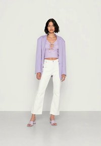 Top cropped de lavanda com detalhe de laço, combinado com jeans brancos de boca de sino e sandálias de deslizar lavanda, contra um fundo claro liso.