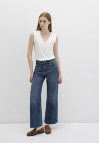 White sleeveless top with a V-neck, blue wide-leg jeans, and brown loafers. Natural fabric texture, casual design, and relaxed fit.
