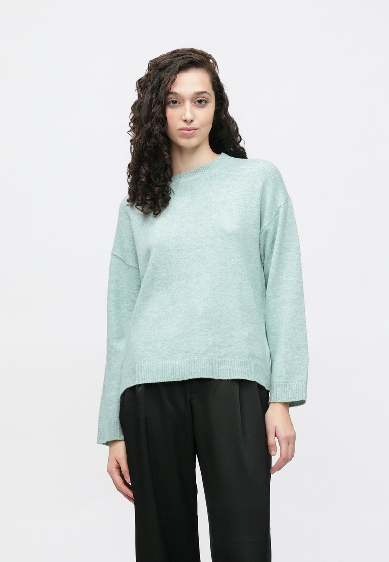 Mintgrønn oversized genser med rund hals, senkede skuldre og ribbestrikkede mansjetter, kombinert med svarte vidbente bukser. Myk tekstur.