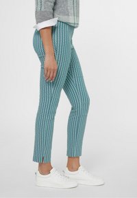 Teal gekleurde broek met een vissenstaartpatroon, met een aansluitende silhouet en openingen bij de enkels. Gepaarde met witte sneakers.