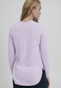 Lila gestrickter Pullover mit langen Ärmeln, abgerundetem Saum und strukturiertem Stoff. Die subtile gerippte Rundhalslinie und die seitlichen Schlitze am Saum sind besondere Merkmale.