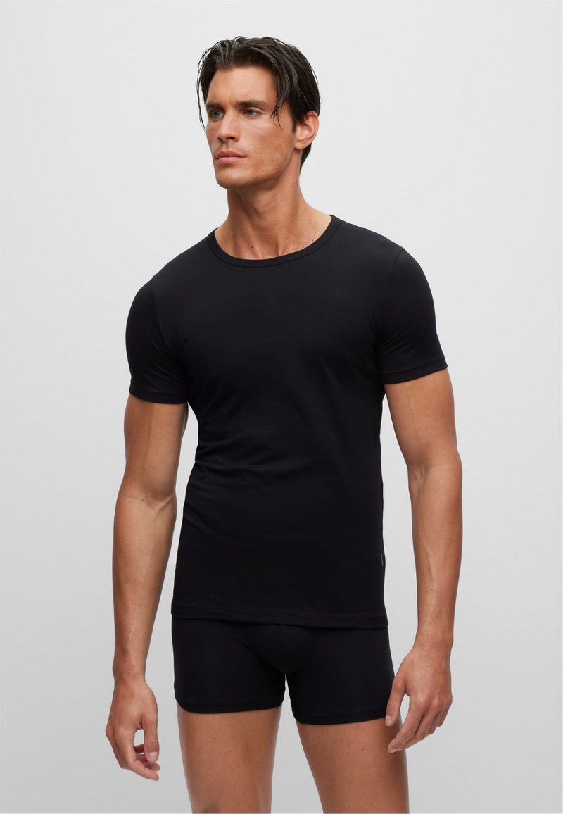 Schwarzes, figurbetontes T-Shirt mit kurzen Ärmeln und Rundhalsausschnitt, aus glatter Stoffqualität; kombiniert mit passenden schwarzen Shorts.