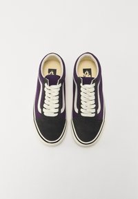 Zapatillas bajas con parte superior de lona morada, puntera de ante negro y cordones blancos, con un logo en blanco y negro en una plantilla color beige.