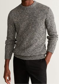 Maglione grigio a maglia con un motivo texture, scollo rotondo e polsini e orlo a coste. Indossato sopra pantaloni neri.