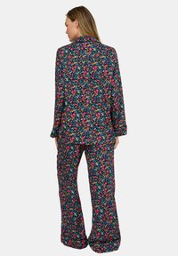 Floral gemustertes Pyjama-Set mit einem langärmeligen Oberteil mit Kragen und ausgestellten Hosen, gefertigt aus weichem Stoff mit dunklem Hintergrund und lebendigen Farben.