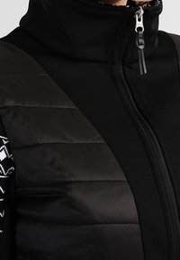 Gilet nero con collo alto che presenta una sezione trapuntata e texturizzata su un lato e tessuto liscio dall'altro, con chiusura con zip e senza motivi visibili.