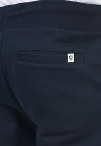 Marinblå joggerbyxor tillverkade av mjukt tyg, med ribbad midja och en enda bakficka med en liten logotagg.