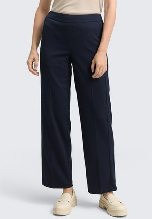 Navy wide-leg pants made from a smooth, lightweight fabric. Features a flat waistband and pressed creases along the legs. Paired with cream loafers.