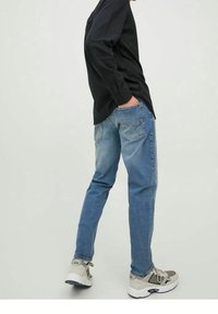 Blå jeans i denim med rak skärning, blekt utseende och stygndetaljer. I kombination med en svart långärmad skjorta och grå sneakers.