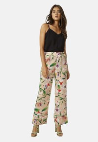 Floral wide-leg pants with a pink background, featuring vibrant blooms in purple, red, and green. Paired with a black sleeveless top.
