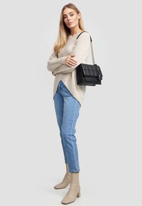 Beżowy sweter z wełny z dekoltem w serek, jasnoniebieskie dżinsy, oraz beżowe botki za kostkę z kwadratowym noskiem. Czarna torebka na łańcuszku z pikowanym wzorem.