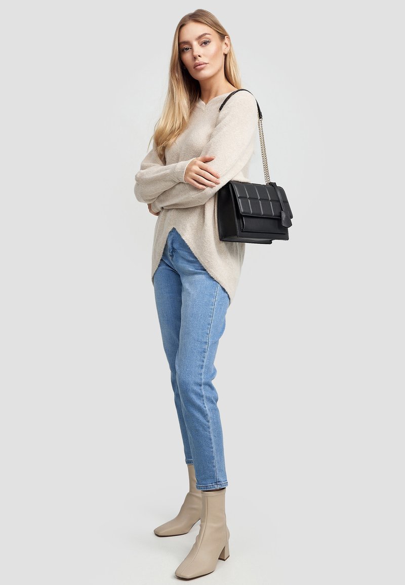 Beżowy sweter z wełny z dekoltem w serek, jasnoniebieskie dżinsy, oraz beżowe botki za kostkę z kwadratowym noskiem. Czarna torebka na łańcuszku z pikowanym wzorem.
