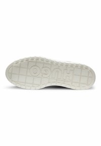 Semelle d'une chaussure blanche avec des crampons profonds et le nom de la marque "HUGO" embossé en grandes lettres sur le dessous.