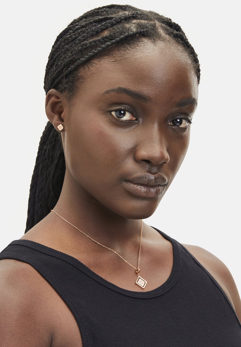 Roséguld halskæde med en firkantet vedhæng, båret af en model. Modellen har flettede hår og har en sort ærmeløs top på.