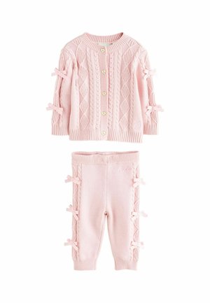 Heled pink kääritud sviiter, millel on teemantimustrid ja südamekujulised nööbid; sobivad püksid külgmiste paelte ja ribatud varrukatega.