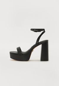 Sandale à plateforme noire avec un épais talon block, une fine bride au niveau de la cheville et une texture en cuir lisse. Design minimaliste avec orteils ouverts.