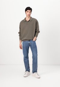Dark green long-sleeve polo shirt paired with light blue straight-leg jeans and white sneakers; smooth fabric and minimal design elements.