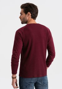 Burgundin pitkähihaisessa t-paidassa on ribbikuvio ja raglan-hihat, jotka on yhdistetty tummaan farkkuun, esittäen mukautuvaa muotoilua.