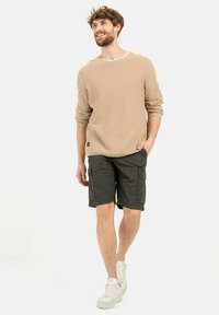 Beige ribbet langærmet skjorte med hvid krave, parret med mørkegrønne cargo shorts. Hvide sneakers fuldender det afslappede outfit.