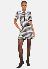 Fekete-fehér kockás ruha rövid ujjakkal, gallérral, fekete részletekkel, arany gombokkal és bővülő alsószoknyával.