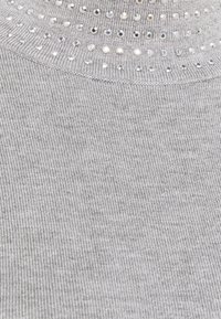 Szara dzianina o prążkowanej strukturze, z srebrnymi ćwiekami ułożonymi w okrągły wzór wzdłuż górnej krawędzi.