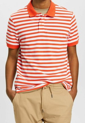 Rood-wit gestreepte poloshirt met een effen oranje kraag; katoenmateriaal; korte mouwen; losse pasvorm. Draagt beige broek.