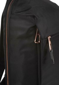 Mochila negra con un tejido texturizado, doble cremallera con herrajes en oro rosa y una silueta elegante. Se puede ver un bolsillo lateral.