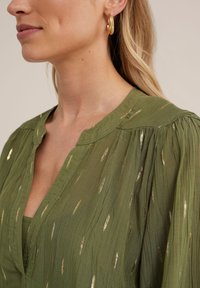 Bluză verde măsliniu cu decolteu în V și mâneci plisate, având accente de fir auriu metalic într-un model de frunze pe un material ușor și texturat.