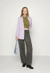 Blazer de lavanda, top crop verde oliva com design geométrico, jeans largos pretos, botas de tornozelo pretas e uma bolsa azul clara.