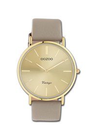 Montre dorée avec un cadran rond, bracelet en cuir beige, marqueurs d'heures minimalistes et inscription "Vintage" sur le visage. Texture lisse, design classique.
