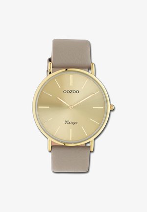 Montre dorée avec un cadran rond, bracelet en cuir beige, marqueurs d'heures minimalistes et inscription "Vintage" sur le visage. Texture lisse, design classique.