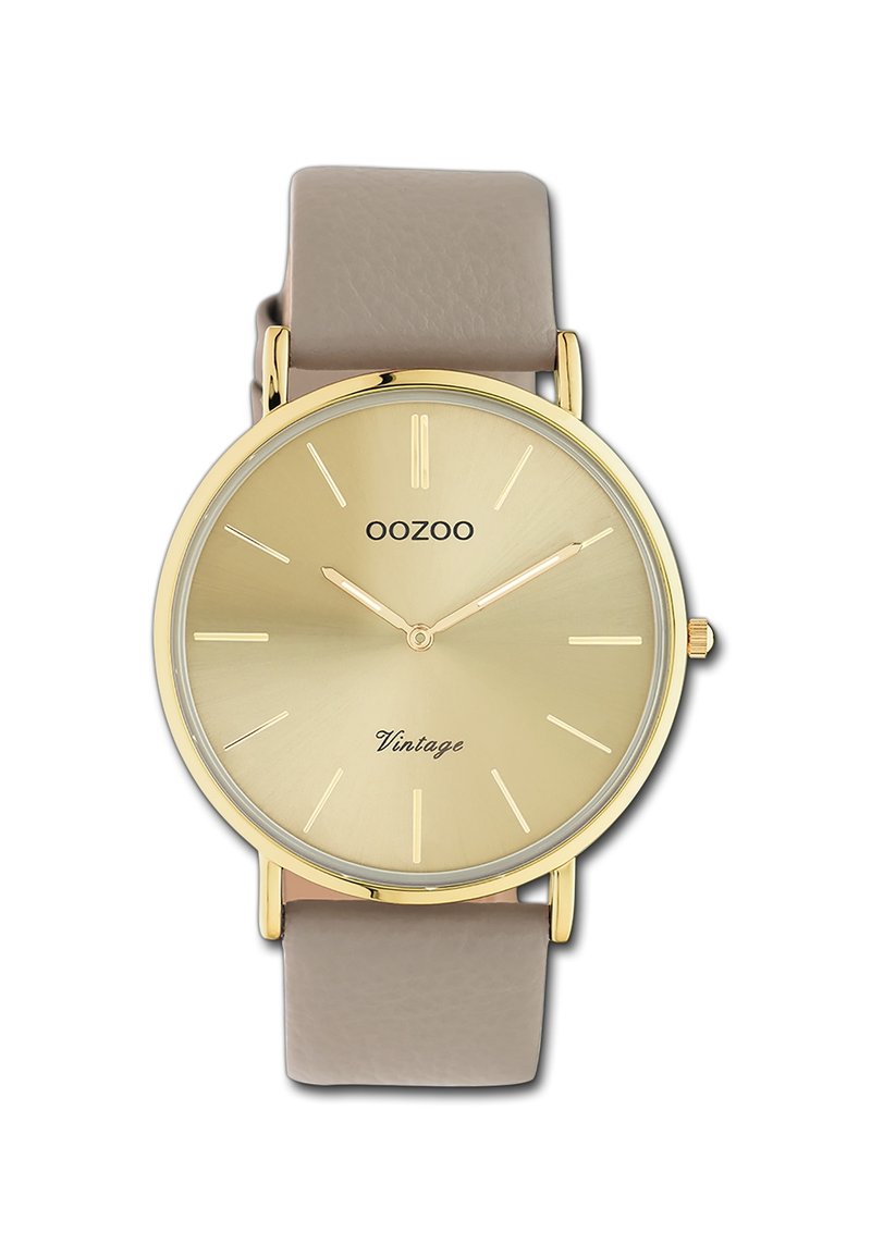 Montre dorée avec un cadran rond, bracelet en cuir beige, marqueurs d'heures minimalistes et inscription "Vintage" sur le visage. Texture lisse, design classique.