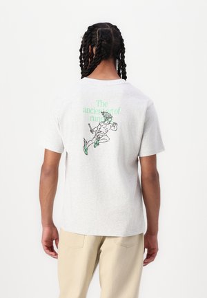 Mann mit geflochtenem Haar, schaut weg, trägt ein hellgraues T-Shirt mit einer grünen Lauf-Figur und dem Text "Die alte Kunst des Laufens."