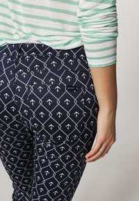 Námořnické kalhoty s bílým vzorem kotev a diamantových tvarů. Mají značkovou etiketu GANT na zadní kapse a hladkou texturu.