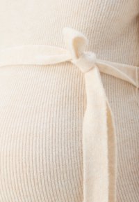 Tessuto a coste beige con una texture morbida, caratterizzato da unaccento con cintura annodata, che crea un aspetto aderente intorno alla vita.