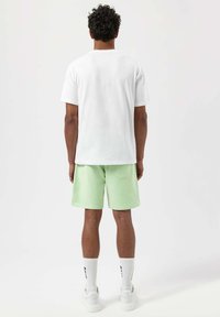 Bílý bavlněný tričko, mátově zelené šortky, bílé tenisky a bílé ponožky s černým nápisem. Jednoduchý, neformální outfit z pohledu zezadu.