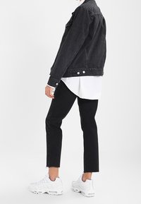 Czarna kurtka dżinsowa z guzikami, w zestawieniu z białą koszulą i czarnymi skróconymi spodniami. Obuwie to białe trampki. Prosty i nowoczesny design.