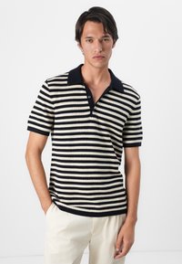 Camisa polo a rayas con textura acanalada, que presenta rayas en navy y crema, un cuello oscuro y dos botones al frente. Manga corta y un ajuste relajado.
