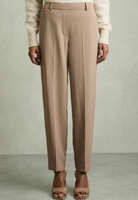 Beige hameidat trouserit, joissa on mukautettu istuvuus, etupleatit ja ei näkyviä taskuja. Kangas on sileäpintainen ja paritettu nude-sandaalien kanssa.