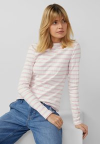 Long-sleeve ribbed t-shirt with pink and white horizontal stripes, featuring a round neckline and fitted design. Paired with blue jeans.