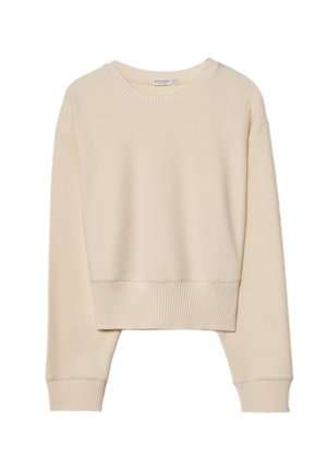 Person wearing a cream sweater with a striped shirt tied around dark jeans, hands covering face, word "SMILE" written on left palm.