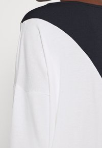 Top a blocchi di colore bianco e blu navy, con una vestibilità rilassata e tessuto in cotone morbido. Il design presenta colori a contrasto sulle spalle.