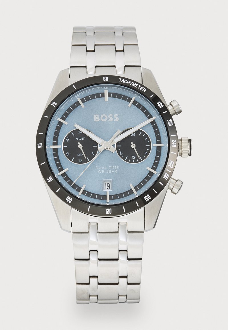 Ceas din oțel inoxidabil cu cadran albastru, bezel tachimetru negru, sub-diale pentru dual time și brățară de ton argintiu. Include o fereastră pentru dată.